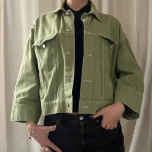 Ljusgrön croppad jeansjacka från Weekday - Säljer en ljusgrön croppad jeansjacka från Weekday med breda ärmar och silverfärgade knappar. Jackan har två bröstfickor med lock och klassisk krage. Perfekt för dig som gillar en avslappnad stil.