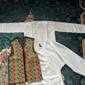 Afghansk traditional klädes set med väst och byxor - Säljer en unik väst med färgglatt broderat geometriskt mönster i rött, grönt, blått och gult. Västen har svarta kanter och är ärmlös, perfekt för att ge din outfit en traditionell och färgstark touch. Inklusive byxor och toppen. För barn/pojkar som är 9-11 år gammal. Oanvänd.