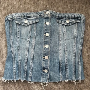 Jeanstopp från Zara - Säljer en snygg jeans topp från Zara i blå denim. Toppen har knappar framtill, två dekorativa fickor vid bysten och rå kant nertill. Baksidan har smock för extra stretch och passform. Perfekt för att lyfta vilken outfit som helst!