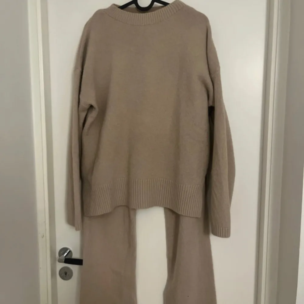 Säljer en beige stickad tröja med rund hals och långa ärmar. Tröjan har breda ribbade muddar vid ärmslut och nederkant. Matchande stickade byxor ingår. Perfekt för en avslappnad och stilren look.. Neuleet.
