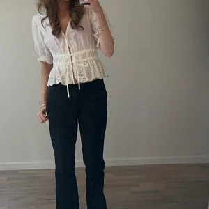 Vit blus med spets och knytband - Säljer en söt vit blus med spetsdetaljer och knytband i midjan. Blusen har v-ringning, korta puffärmar och volangkant nertill. Använd endast fåtal gånger.