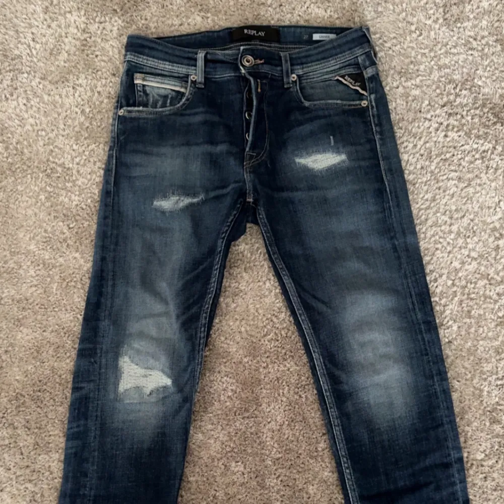 Säljer ett par snygga mörkblå Replay jeans med slitna detaljer och klassisk femficksdesign. Jeansen har knappar i gylfen och en läderpatch bak i midjan. Perfekta för dig som gillar en avslappnad men stilren look. Storlek W27 L32. Farkut & Housut.