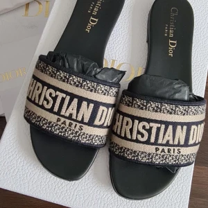 Christian Dior sandaler med logga - Snygga sandaler från Christian Dior med bred beige och svart rem där loggan 'CHRISTIAN DIOR PARIS' är broderad. Platt sula och öppen tå, perfekt för varma dagar. Klassisk och lyxig design som sticker ut.
