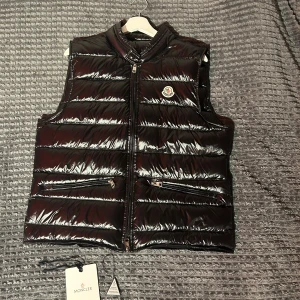 Svart dunväst från Moncler - Säljer en glansig svart dunväst från Moncler med dragkedja framtill och Moncler-logga på bröstet. Västen har ståkrage och två fickor med dragkedja. Perfekt för lager-på-lager och snygg till många outfits. Storlek 3 vilket motsvarar Large. Men är kort så sitter mer som S\M. Skick 9,5 utan 10. Har tappat bort den triangel saken som bevisar äkthet men har kvar tagen. nfc och Qr kod funkar. Ganska säker på att detta är en lite gammlare model. Hör av dig om du undrar något👍