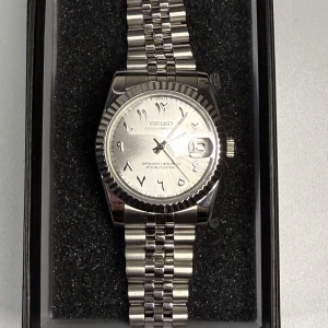 Seiko Datejust 36mm ( Arabic Dial ) - Elegant och tidlös Seiko Datejust i 36 mm med unik arabisk urtavla – en klocka som kombinerar stil med funktion. Utrustad med reptåligt safirglas både fram och bak, vilket ger extra hållbarhet och exklusiv känsla. Klockan är vattentät och har en tydlig datumvisning för extra bekvämlighet. Länken är enkelt justerbar för att passa din handled perfekt.