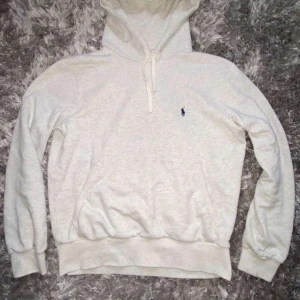 Grå hoodie från Polo Ralph Lauren - Säljer en klassisk vit hoodie från Polo Ralph Lauren med liten broderad logga på bröstet. Tröjan har huva med dragsko och en stor magficka. Perfekt för en avslappnad stil.
