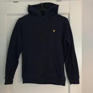 Mörkblå hoodie från Lyle & Scott - Säljer en mörkblå hoodie från Lyle & Scott med klassisk gul logga på bröstet. Tröjan har huva, lång ärm och en stor magficka framtill. 