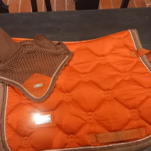 Brun och orange ridhuva från Equestrian Stockholm - Snygg brun och orange ridhuva från Equestrian Stockholm. Huvan är virkad med tyg över öronen och har en dekorativ kant i silver. Perfekt för ridning och matchar schabrak i samma färg. Finns lite slitage men i bra skick