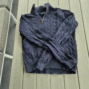 Intresskoll ralph laureb halfzip kabelstickad  - Säljer en mörkblå stickad tröja från Polo Ralph Lauren med dragkedja vid halsen och klassiskt kabelstickat mönster. Tröjan har lång ärm och broderad logga på bröstet. Perfekt för lager-på-lager under kyliga dagar. Passar xs - s