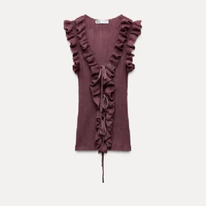 Plommonlila volangtopp med djup v-ringning - Supersnygg plommonlila topp från Zara med volangdetaljer längs v-ringningen och axlarna. Toppen är ärmlös och har knyt framtill. Perfekt för dig som vill sticka ut med en trendig och feminin look.