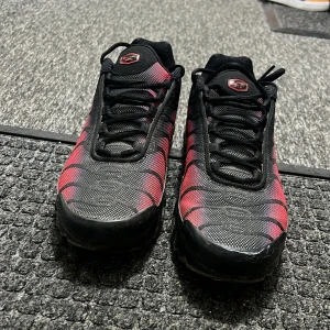 Nike Air Max Plus TN röd och svart - Säljer ett par Nike Air Max Plus TN i rött och svart med klassiska vågiga linjer och svarta detaljer. Skorna har snörning, mesh-överdel och synlig Air Max-dämpning i sulan. Perfekta för dig som vill sticka ut med en sportig look.