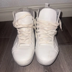 Vita höga sneakers med snörning - Säljer ett par klassiska vita höga sneakers från KIFO med snörning. Skorna har en stilren design med rund tå och platt sula, perfekta för en clean och enkel look. Passar till många olika outfits och är riktigt bekväma.
