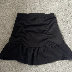 Svart kjol med volang från Gina Tricot - Supersnygg svart kjol från Gina Tricot med volang nertill och lätt rynkade sidor. Kjolen har en kort längd och är tight