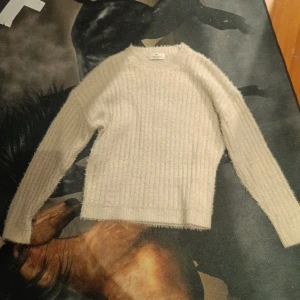Vit fluffig stickad tröja från H&M - Mysig beige stickad tröja från H&M med fluffig känsla. Tröjan har rund halsringning och långa ärmar, perfekt för kyliga dagar. Enkel och stilren design som passar till det mesta.