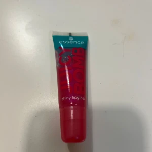 Essence Juicy Bomb Lipgloss - Juicy Bomb shiny lipgloss från Essence i färgen 102 Witty Watermelon. Kommer i en smidig tub med turkos och röd design. Ger glansiga, saftiga läppar med en hint av rosa-röd ton och fruktig känsla. Perfekt för dig som vill ha en glansig finish.