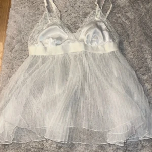 Vit nattlinne  från Hunkemöller - Supersöt och snygg topp/nattlinne från Hunkemöller med tunna axelband, spetsdetaljer upptill och plisserad mesh i nertill. Överdelen är i glansigt material med spetskant, vilket ger en romantisk vibe. Perfekt för dig som gillar feminina och lätta plagg. Perfekt och snygg nattlinne