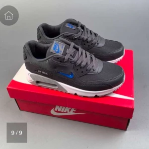 Nike Air Max 90 grå/blå sneakers - Snygga Nike Air Max 90 sneakers i mörkgrått med blå detaljer och vit sula. Skorna har klassisk snörning, rund tå och är tillverkade i syntet och textil. Perfekta för dig som gillar streetstyle och vill ha en ikonisk sneaker med skön dämpning.