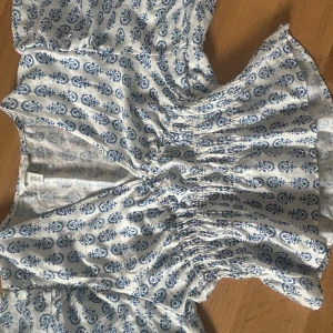 Vit och blå blus med mönster från Hm - Supersöt blus från Hm i vitt med blått blommigt mönster.  Blusen har omlott-v-ringning, smockad midja och trekvartsarm . Perfekt för varma dagar och har en lätt och luftig känsla tack vare bomullsmaterialet.