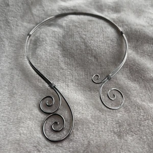 Silvrigt halsband med spiraldesign - Unikt halsband i silverfärgad metall med coola spiralformade detaljer i båda ändar. Sitter snyggt runt halsen och ger en edgy vibe till din outfit. Perfekt för dig som gillar statement-smycken och vill sticka ut med något annorlunda.