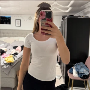 Vit basic t-shirt med rund hals - Enkel och fräsch vit t-shirt med rund halsringning och korta ärmar. Sitter tight och är perfekt att styla med jeans eller kjol. Gjord i mjukt bomullsmaterial som känns skönt mot huden.