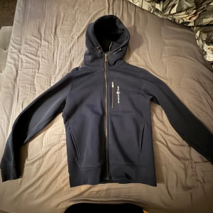 Mörkblå hoodie från Sail racing  - Snygg mörkblå hoodie från Sail racing med dragkedja hela vägen och huva med snörning. Använd ett par gånger, inga defekter 