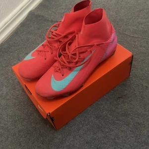 Nike Superfly 10 fotbollsskor orange - Nike Superfly 10 fotbollsskor i en riktigt snygg orange färg med ljusgröna detaljer och stor Swoosh på sidan. Skorna har snörning, högre skaft och platt sula med dobbar för bra grepp på planen. Perfekta för dig som vill sticka ut på matchen!