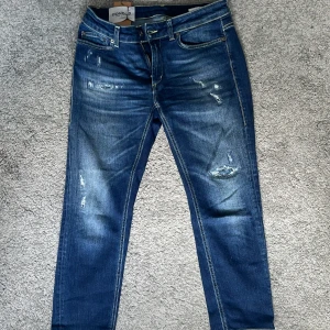 Slitna jeans från Dondup,  - Snygga blå jeans från Dondup med slitna detaljer och klassisk femficksdesign. Jeansen har normal passform, raka ben och tydliga kontrastsömmar. Tillverkade i jeansmaterial och har en läderpatch med logga bak i midjan. Modellen heter Monroe! Hör av dig för minsta lilla fråga📬
