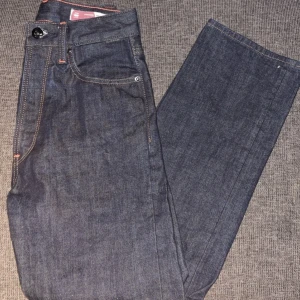 G-Star RAW Jeans - Snygga mörkblå jeans från G-Star RAW med klassisk femficksdesign och orange kontrastsömmar. Jeansen har rak passform och är tillverkade i slitstarkt denimtyg. Perfekta för dig som gillar en stilren och tidlös look.