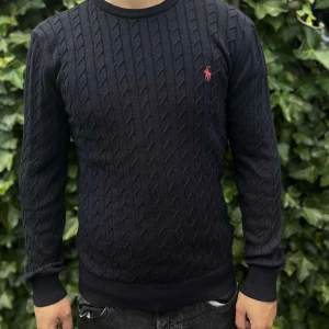 Svart kabelstickad tröja Polo Ralph Lauren - Marinblå kabelstickad tröja från Polo Ralph Lauren med klassisk rund hals och röd broderad logga på bröstet. Tröjan är långärmad och har ribbade muddar vid ärmslut och nederkant. Perfekt för dig som gillar stilren och tidlös design..   .    Nypris: 2395kr GORILLAPRIZE:1160kr             Skick:10/10 oöppnad          KVITTO MEDKOMMER  