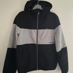 Jack and Jones windbreaker  - Säljer en svart/grå windbreaker från Jack and Jones. Den är helt ny och i perfekt skick. Storlek är xs och hör av er vid frågor.