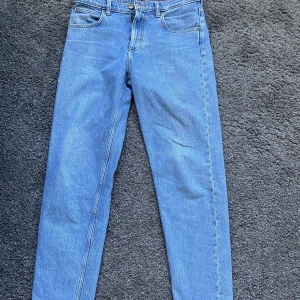 Blå Lee jeans Oscar W29 L32 - Säljer ett par klassiska blå jeans från Lee, modell Oscar. Jeansen har fem fickor, raka ben och normal passform. Tillverkade i slitstarkt denimtyg av bomull. Perfekta för dig som gillar en tidlös look med enkel stil. Jeansen har en liten slitning på höger ben vilket syns på bilden!