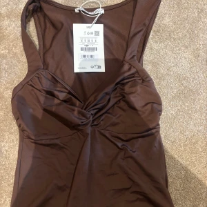 Brun twistad topp från Pull&Bear - Supersnygg brun linnetopp från Pull&Bear med twistad detalj framtill och breda axelband. Helt ny. Köpt för 400 kr.