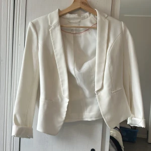 Vit kavaj från H&M - Snygg vit kavaj från H&M i storlek 36. Kavajen har klassisk krage, figurnära passform och två fickor framtill. Materialet är slätt och känns mjukt, med ett stilrent och fräscht uttryck. Perfekt att styla med jeans eller kostymbyxor för en clean look.