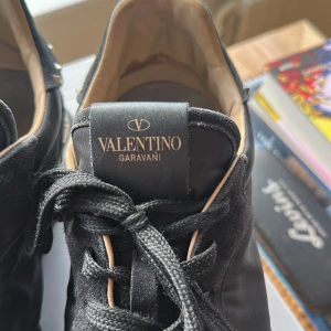 Valentino Garavani svarta sneakers - Har ej original innersulor. Svarta Valentino Garavani sneakers med coola nitar runt sulan och hälen. Skorna har snörning, rund tå och platt sula. Materialmix av mocka och syntet ger en lyxig känsla. Perfekt för dig som gillar edgy designerstil och vill sticka ut med detaljer.