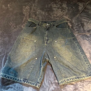 Vision Street Wear jeansshorts M - Säljer ett par loose-fit jeansshorts från Vision Street Wear i klassisk mörkblå denim. Modellen har elastisk midja, dragkedja och knapp, samt stora fickor både fram och bak. Perfekt för dig som gillar streetstyle och skön passform.