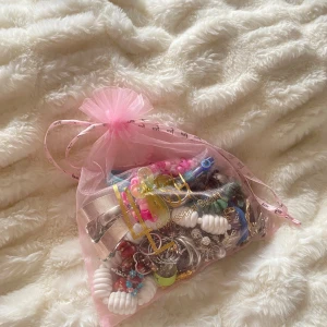 Stort smyckespaket i rosa påse - Ett mixat smyckespaket med massor av färgglada armband, ringar och örhängen i olika former och material. Här finns pärlor, plast, metall och detaljer i guld och silver. Perfekt för dig som gillar att variera din stil och mixa färger som blått, grönt, rosa och vitt🌸🌸