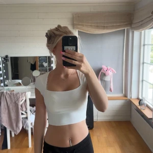 Vit croppad topp med kort ärm - Snygg vit croppad topp med fyrkantig ringning och korta ärmar. Perfekt för varma dagar och enkel att matcha med både jeans och kjol. Toppens stilrena design gör den till ett måste i garderoben för dig som gillar trendiga basplagg.