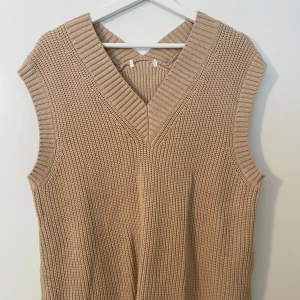 Beige stickad väst med v-ringning - Säljer en beige stickad väst med bred v-ringning och grov ribbad struktur. En loose passform gör den enkel att styla över en t-shirt eller skjorta. Perfekt för lager-på-lager. Storlek M/L