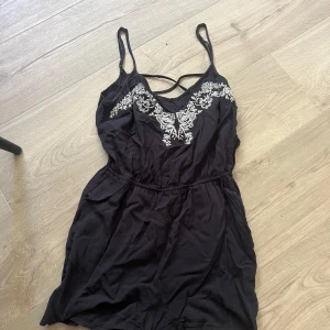 Svart kort jumpsuit med broderi - Säljer en marinblå kort jumpsuit med tunna reglerbara axelband och snygga korsade band över ryggen