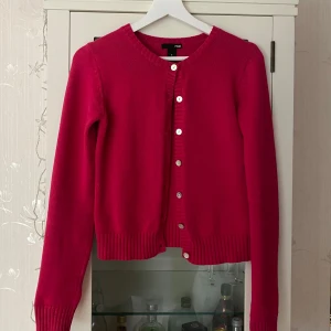 Ceriserosa kofta från H&M, storlek S - Superfin ceriserosa kofta från H&M i storlek S. Koftan har rund hals, långa ärmar och silvriga knappar framtill. Ribbstickade muddar vid ärmslut och nederkant. Perfekt att slänga över en topp för en färgklick i din outfit!