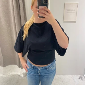 Poncho topp - Säljer en svart croppad topp med vida, nästan trekvartsärmar och rund halsringning. Toppen har en enkel och stilren design som är lätt att matcha med olika outfits. Perfekt för dig som gillar en avslappnad men trendig look.
