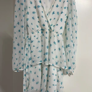 Vit blommig omlottklänning Gina Tricot - Priset kan sänkas. I superbra skick använd bara 1 gång. Supersöt vit omlottklänning från Gina Tricot med blå blommor och lång ärm. Klänningen har v-ringad hals och ett luftigt, lätt material som ger en flowy känsla. Perfekt för dig som gillar romantiska och fräscha vibes. Passar dig som vill ha en feminin look med lite extra detaljer.