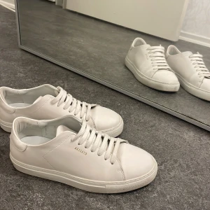 Vita sneakers från Axel Arigato - Stilrena vita sneakers från Axel Arigato med minimalistisk design och diskret logga på sidan. Skorna har rund tå, platt sula och klassisk snörning. Tillverkade i slätt skinn för en clean look som passar till allt. Kommer med skopåse och kartong.