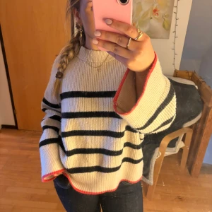 Randig stickad tröja från Zara - Säljer en beige stickad tröja från Zara med svarta ränder och röda detaljer nedtill. Tröjan är tjock och mysig perfekt till hösten. I storlek M💘