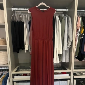 Vinröd långklänning - Snygg vinröd långklänning med rund hals och ärmlös design. Klänningen har ett markerat midjeparti och ett mjukt, fallande tyg. Jätte fint skick!