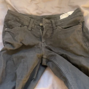 Lågmidjade Svarta bootcut jeans från Vero Moda - Svarta jeans från Vero Moda med klassisk femficksdesign och bootcut-ben. Byxorna har normal midja, dragkedja och knapp framtill. Materialet är mjukt och stretchigt, perfekt för en chill och snygg look.