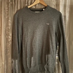 Grå tröja från gant - Snygg grå tröja från gant med klassisk rund halsringning och diskret broderad logga på bröstet. Långärmad modell i mjuk bomull, perfekt för lager-på-lager och chill stil.