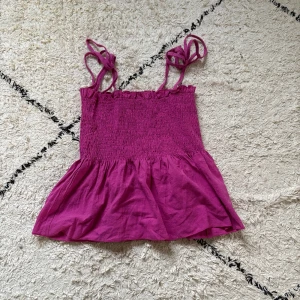 Rosa linnetopp från Shein - Supersöt rosa linnetopp från Shein i storlek XS. Toppen har smockad överdel, volangkant nedtill och tunna axelband som knyts upptill. Perfekt för varma dagar och ger en riktigt somrig vibe. Materialet känns lätt och luftigt.