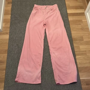Rosa jeans från H&M Divided - Snygga rosa jeans från H&M Divided i storlek 38. Byxorna har raka, vida ben och klassisk femficksdesign. Tillverkade i mjuk bomullsmix med skön känsla och bälteshällor i midjan. Perfekta för dig som vill sticka ut med färg. Liten fläck på vänstra byxbenet.