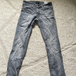 Grå slim jeans Jack & Jones Glenn - Slim fit jeans från Jack & Jones i modellen Glenn. Snyggt ljusgrå tvätt med klassiska fem fickor och dragkedjegylf. Jeansen är i bomullsmix och har en modern, smal passform som sitter snyggt längs benen.